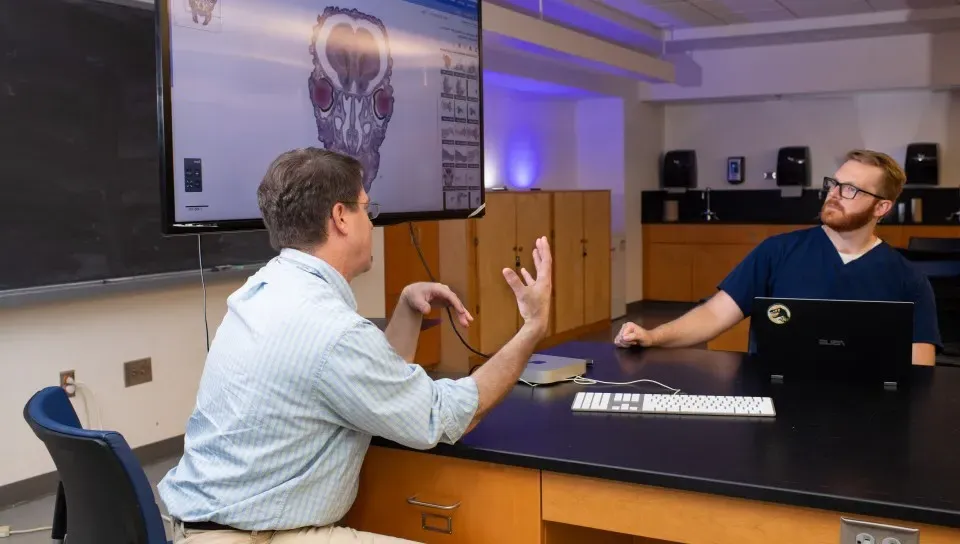 A professor speaks with a student in a classroom